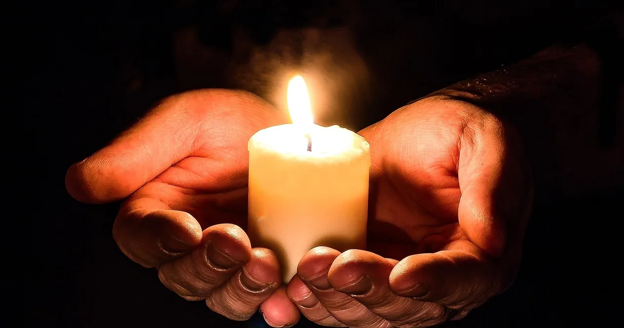 Mãos em concha segurando uma vela acesa no escuro, carta de Deus para um dependente químico