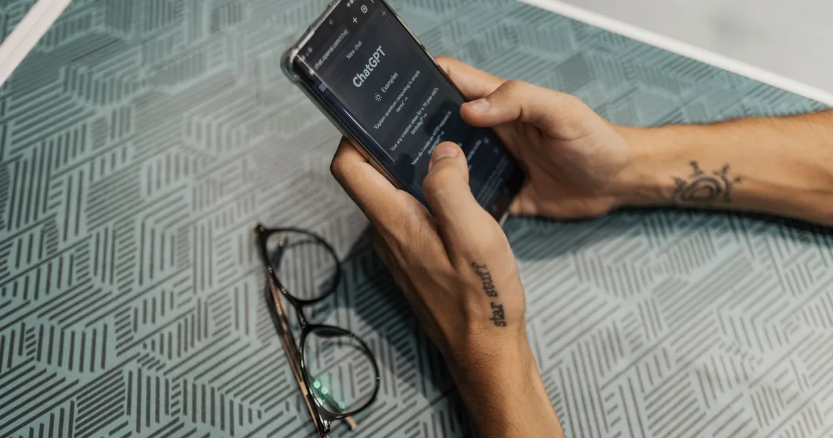 Mãos segurando um celular com a tela desligada sobre a mesa, regras para usar celular em clínica de reabilitação