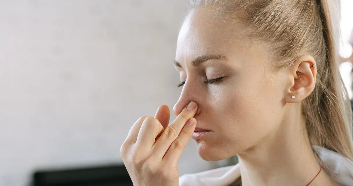 Mulher apertando o nariz com os dedos e olhos fechados, cocaína tem cheiro e como identificar pelo odor