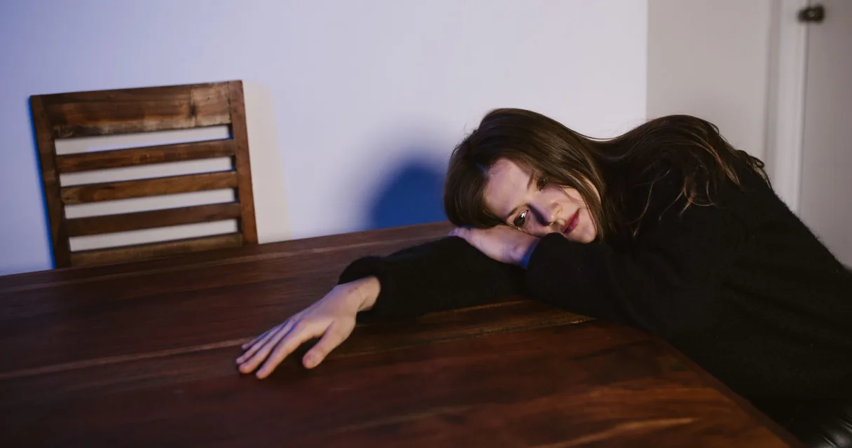Mulher deitada sobre a mesa da cozinha com expressão de tristeza à noite, desabafo de esposa de dependente químico