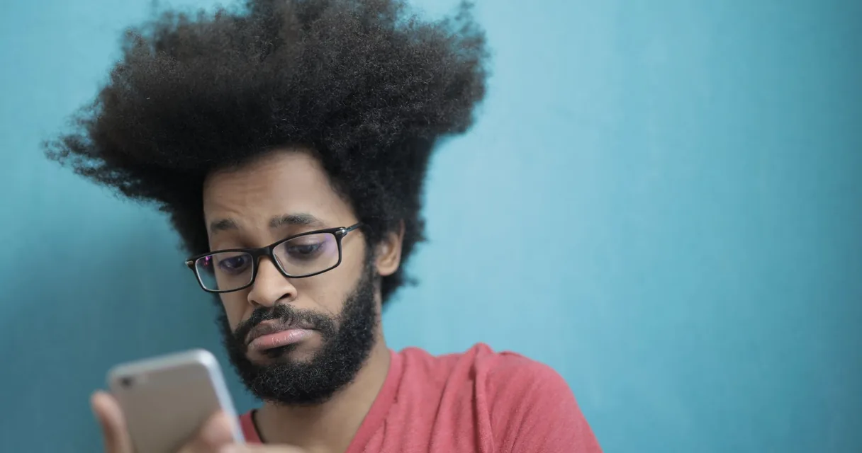 Homem de óculos olhando fixamente para o celular com expressão ansiosa, vício em dopamina
