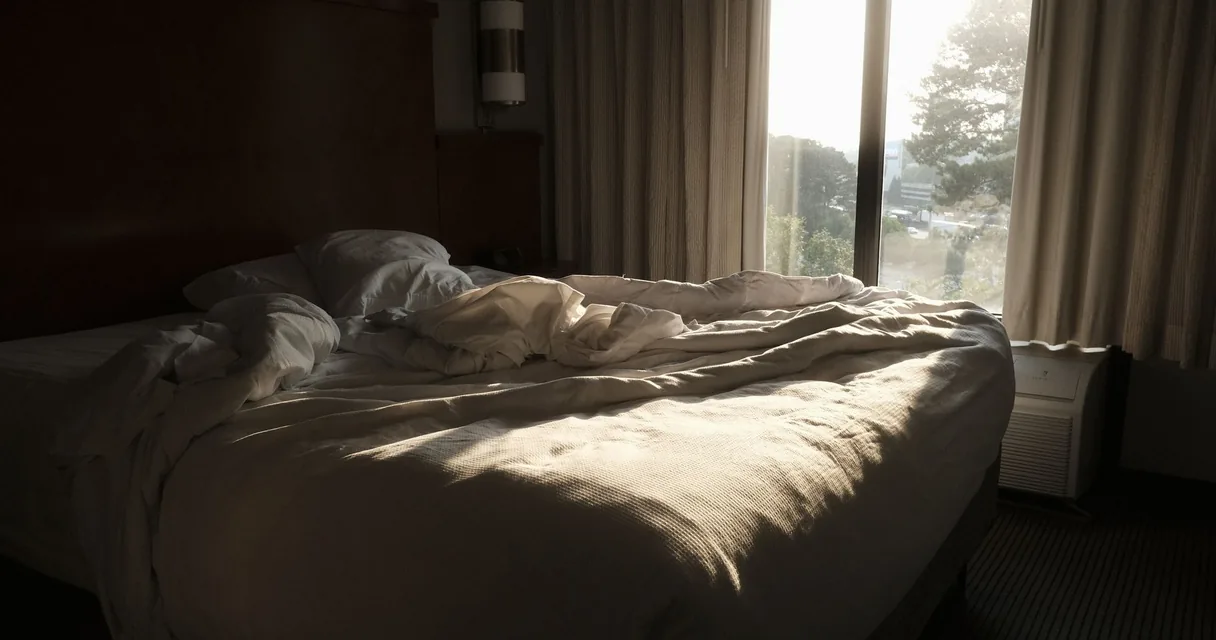 Cama desfeita com lençóis amassados à luz da manhã, vício em sexo e compulsão
